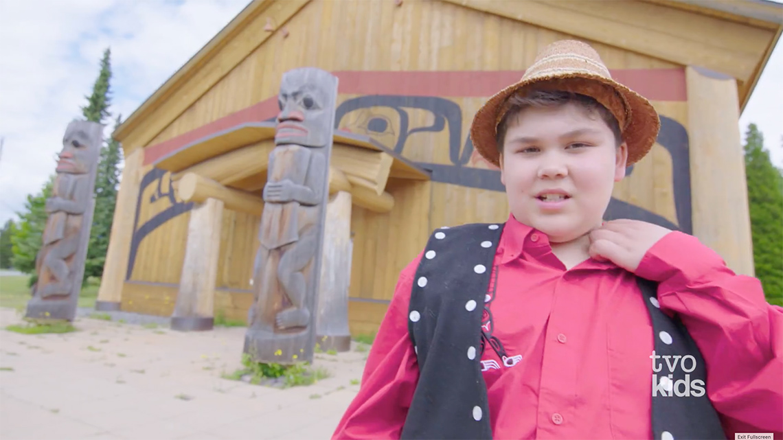 Drakon is standing outside a Tsimshian longhouse.
