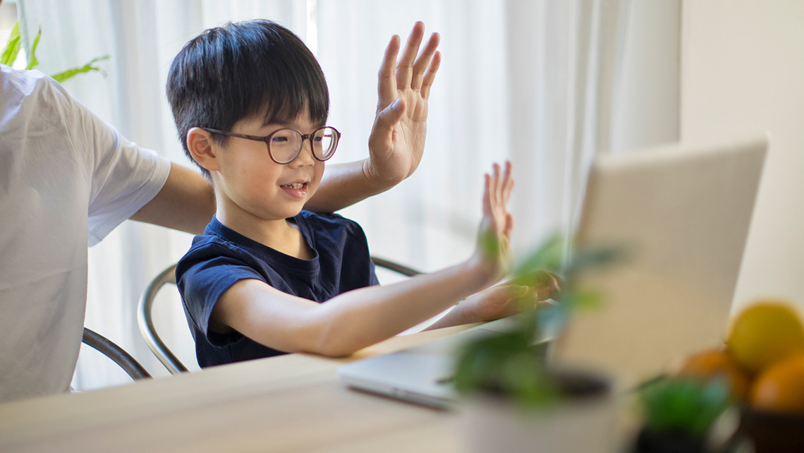 A child is doing a video call on a laptop with an adult next to them.