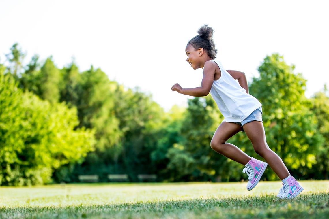 A child is running on a paved footpath.