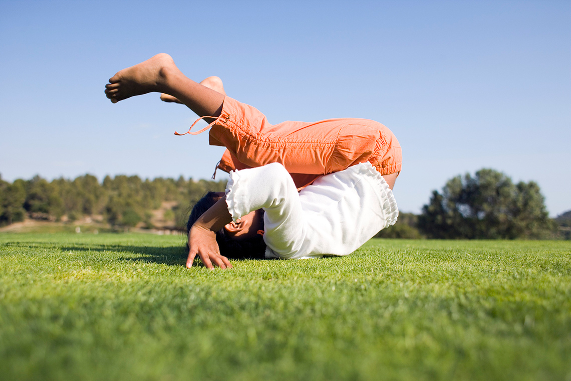 A child is rolling on their back on a grassy field.