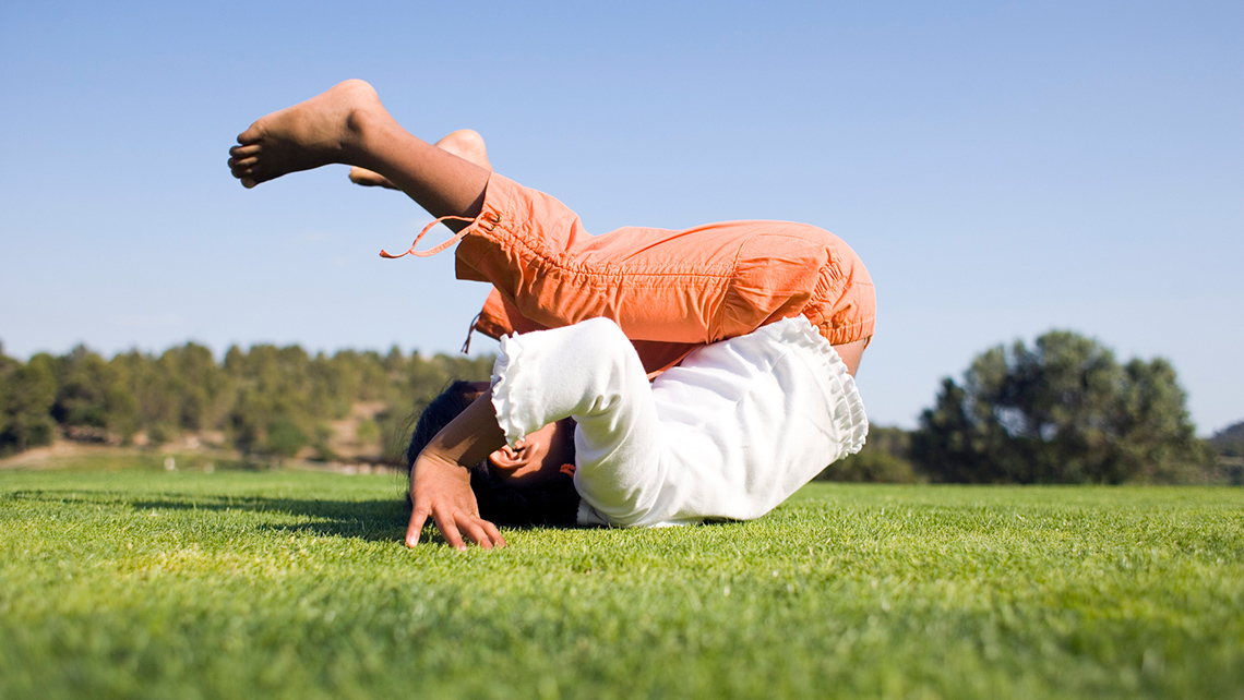 A child is rolling on their back on a grassy field.