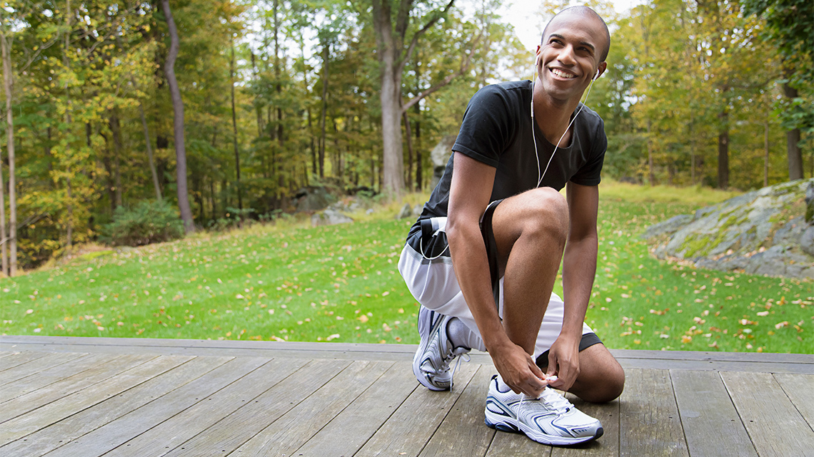 A person is kneeling on one knee and tying their shoelace.