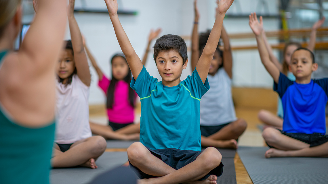 A group of children are stretching with their arms in the air.