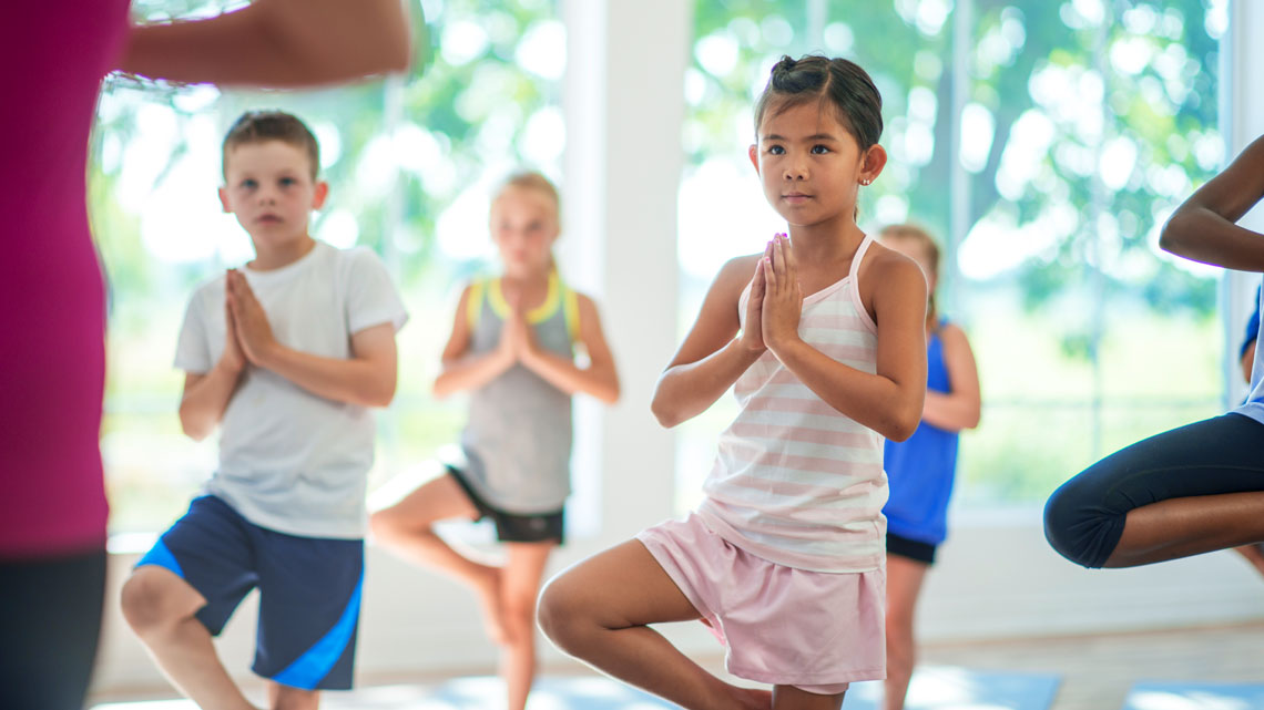 A person is standing balanced on one leg with arms bent and palms touching