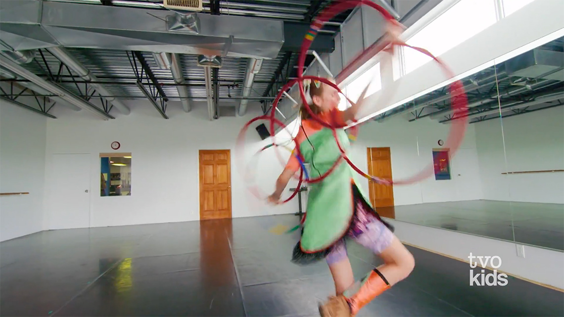 Emily dancing in a studio. She has 6 hoops behind her back and is forming a butterfly.