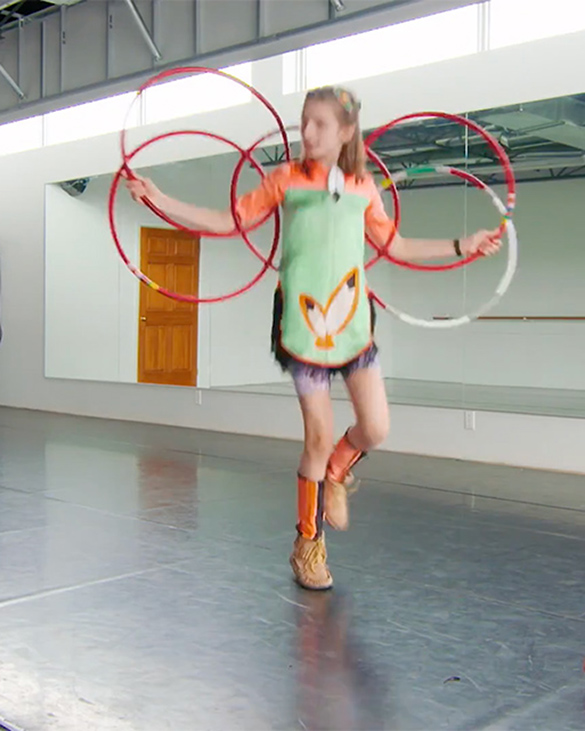 Emily dancing with hoops. She is standing with 3 hoops on her back and her feet kicking outward. 