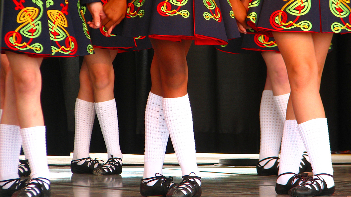 A group of dancers are wearing traditional Irish step dancing costumes with Ghillies (soft shoes) on their feet. 