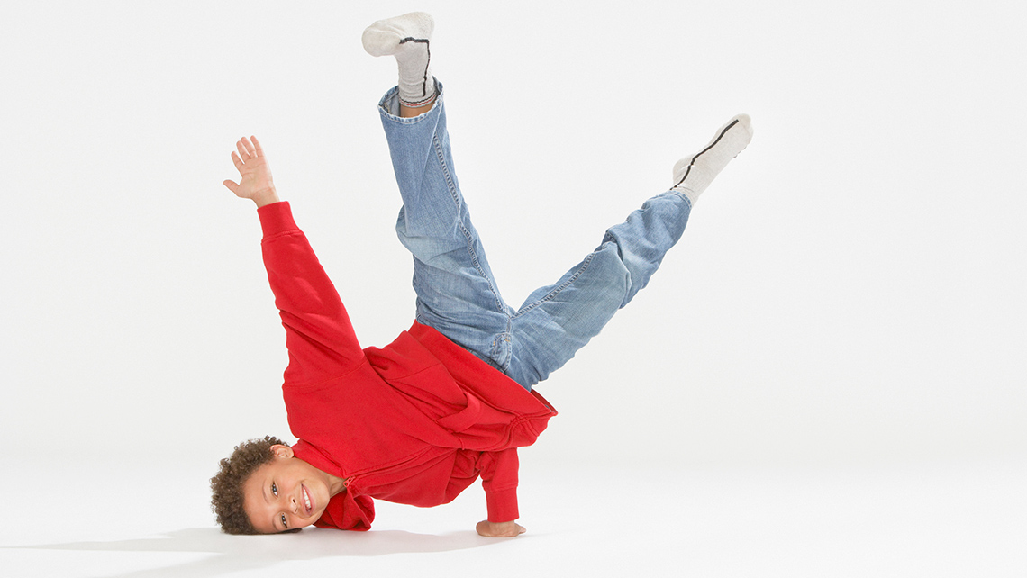 A child is breakdancing. The side of their head is on the ground and one hand is supporting the rest of their body.