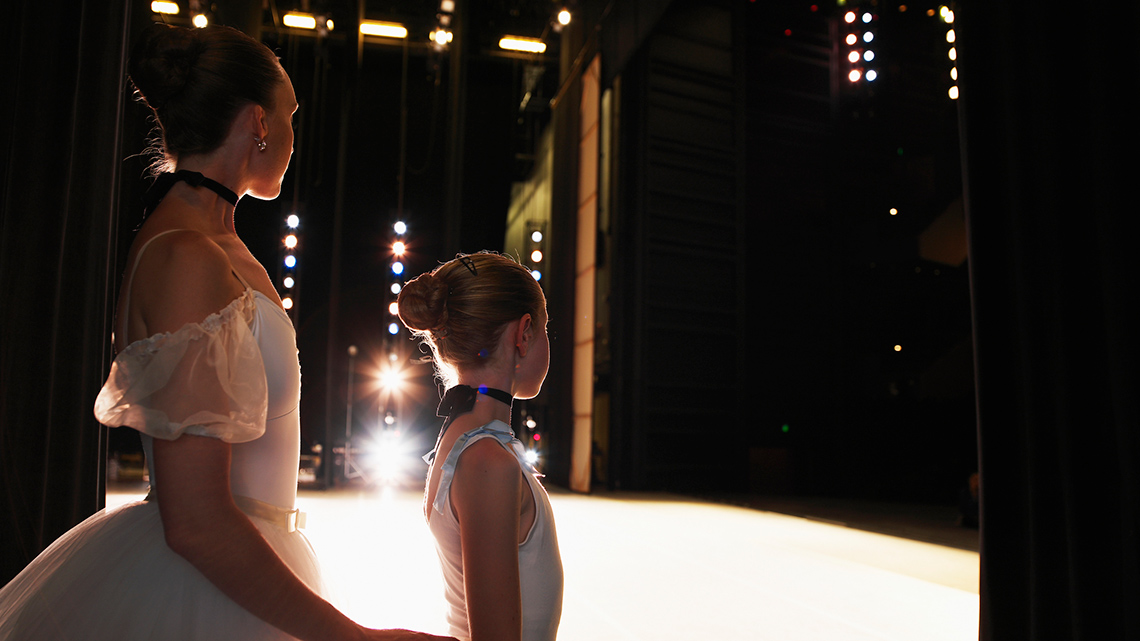 An adult and a child are off stage with their sides to the camera. The audience cannot see them.
