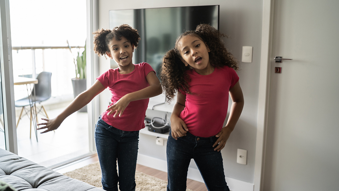Two children are dancing beside each other. They are wearing similar outfits and are doing similar dance movements.