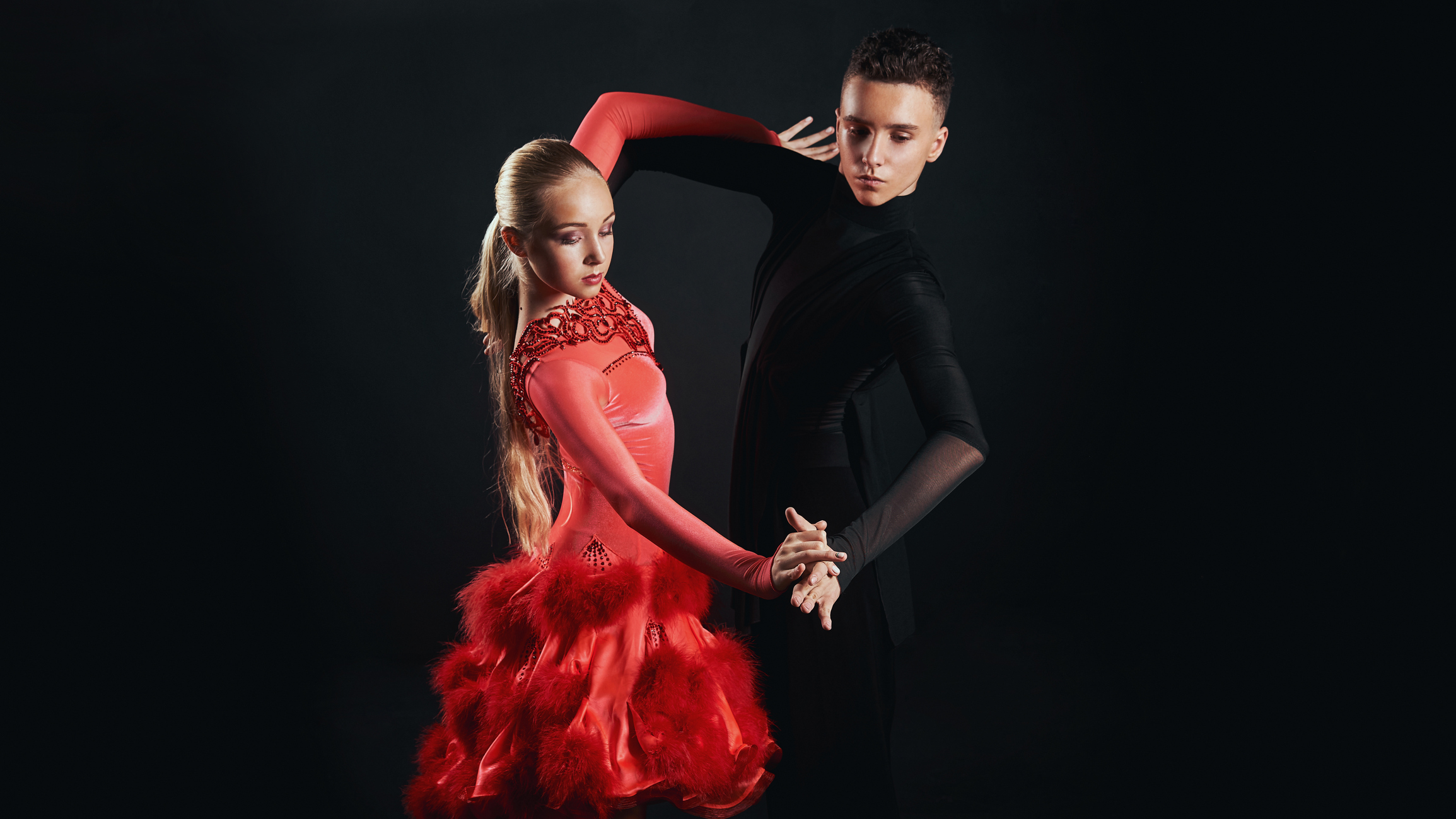 Two individuals dressed formally and dancing the salsa on a stage.