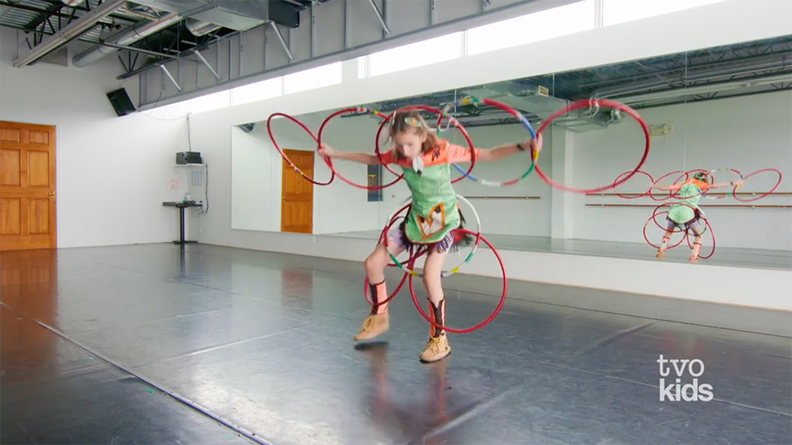 Child dressed in regalia, while using many hoops to dance.