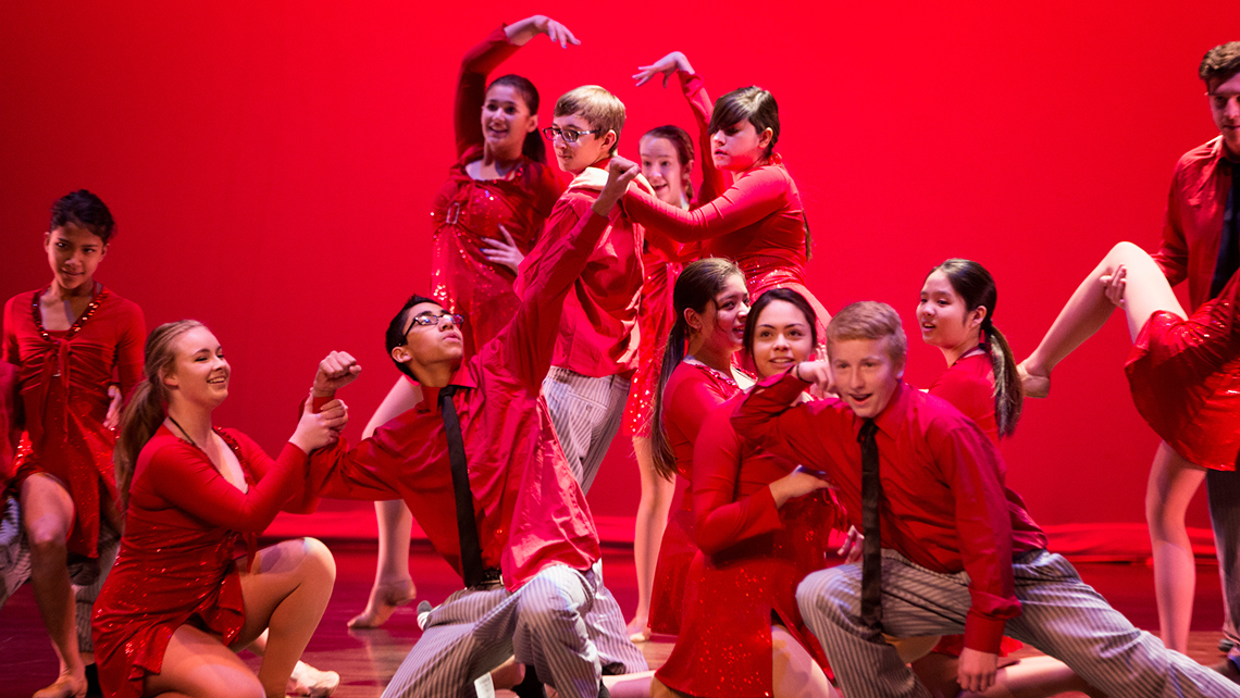 Stage dancers dressed in red and holding a final pose.