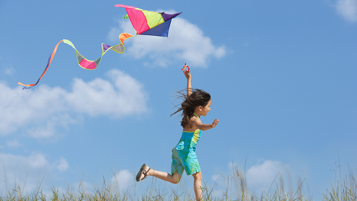 Child running while flying a kite on a windy day. 