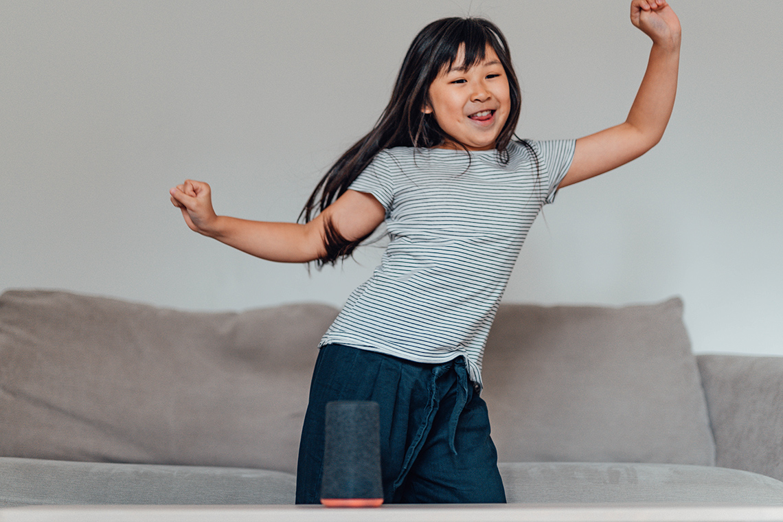 dancing A young person stands in front of a couch indoors dancing in place, swinging their hips back and forth and moving their arms up and down.