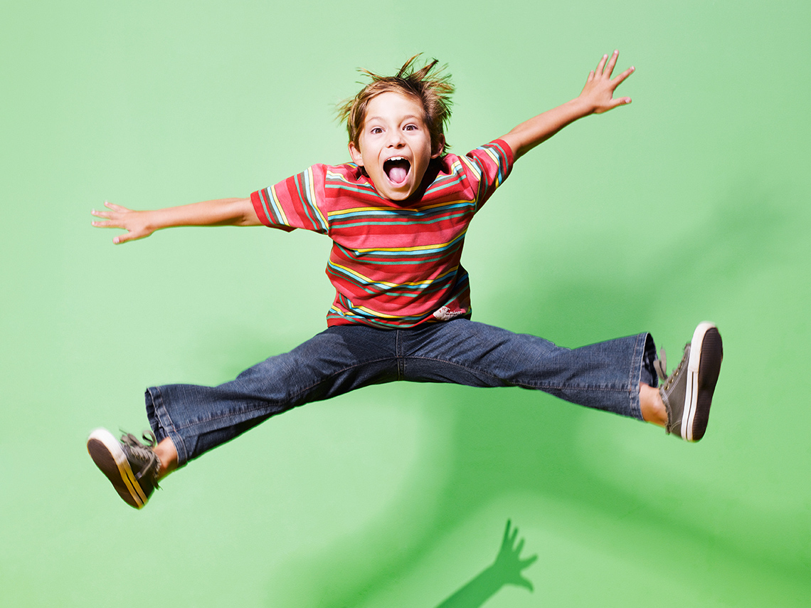 A young person wearing casual clothes jumps into the air with their legs spread apart and their arms held out at shoulder height.