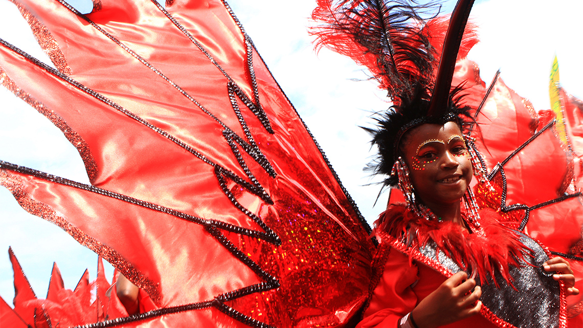 A Toronto Carnival participant wears a feathered headdress with a beak, a sequined top, and big colourful wings.
