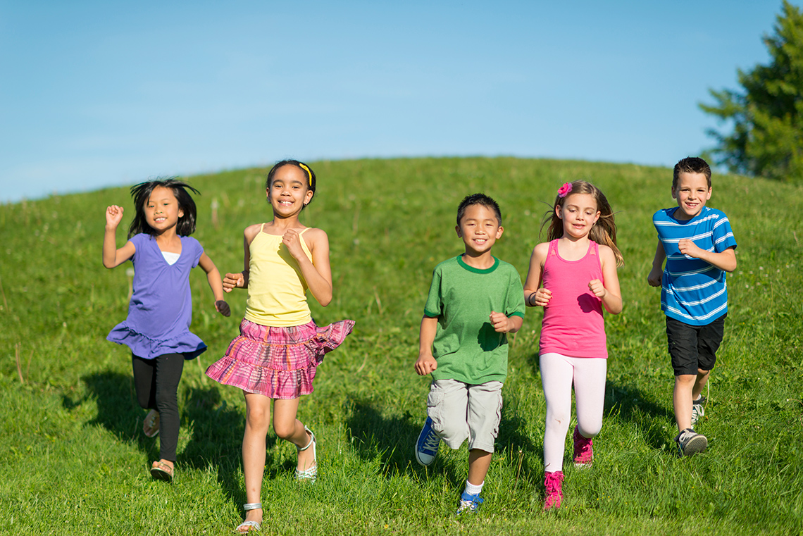 Creating movements Five young people, all in a row and smiling, run excitedly towards you down a grassy hill outdoors on a sunny day.