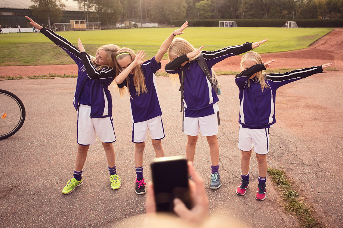 Dance trends Four students do the dab dance move outdoors, their heads tucked into the crook of 1 bent arm covering their faces, 1 arm held straight out.