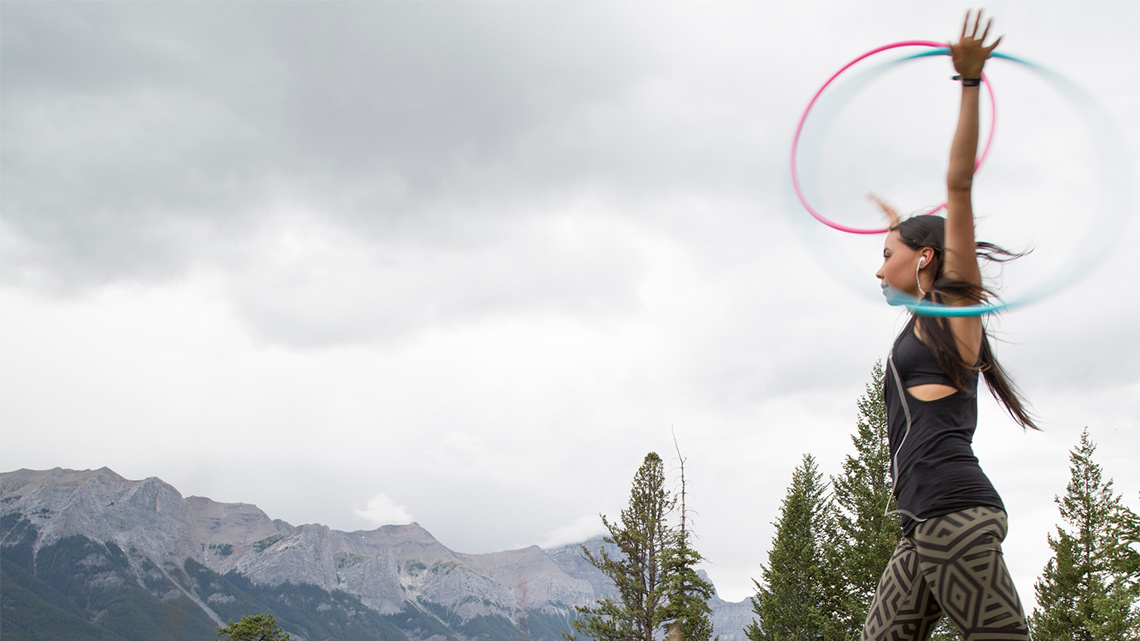 An Indigenous dancer is circling two coloured hoops on their arms.