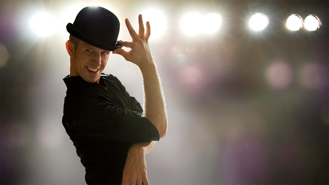 A jazz dancer holds the brim of a bowler hat between their thumb and forefinger.