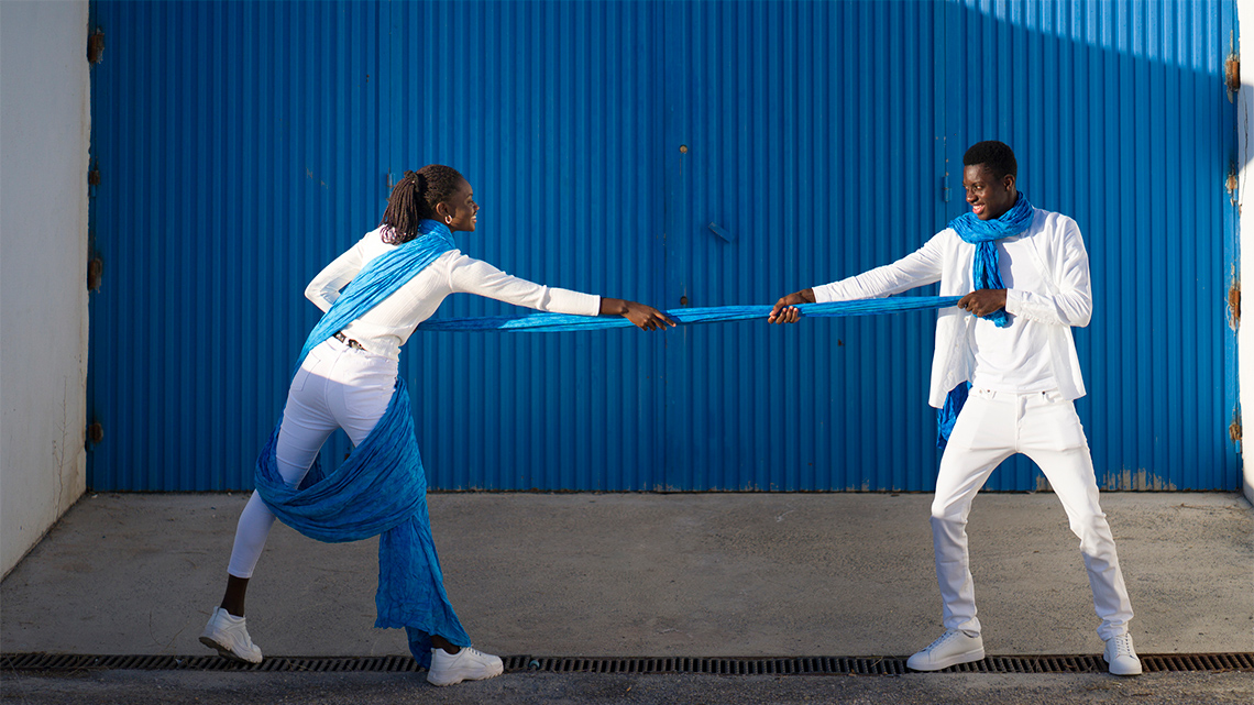 Two dancers are pulling a blue piece of fabric between them, as if in a tug of war.