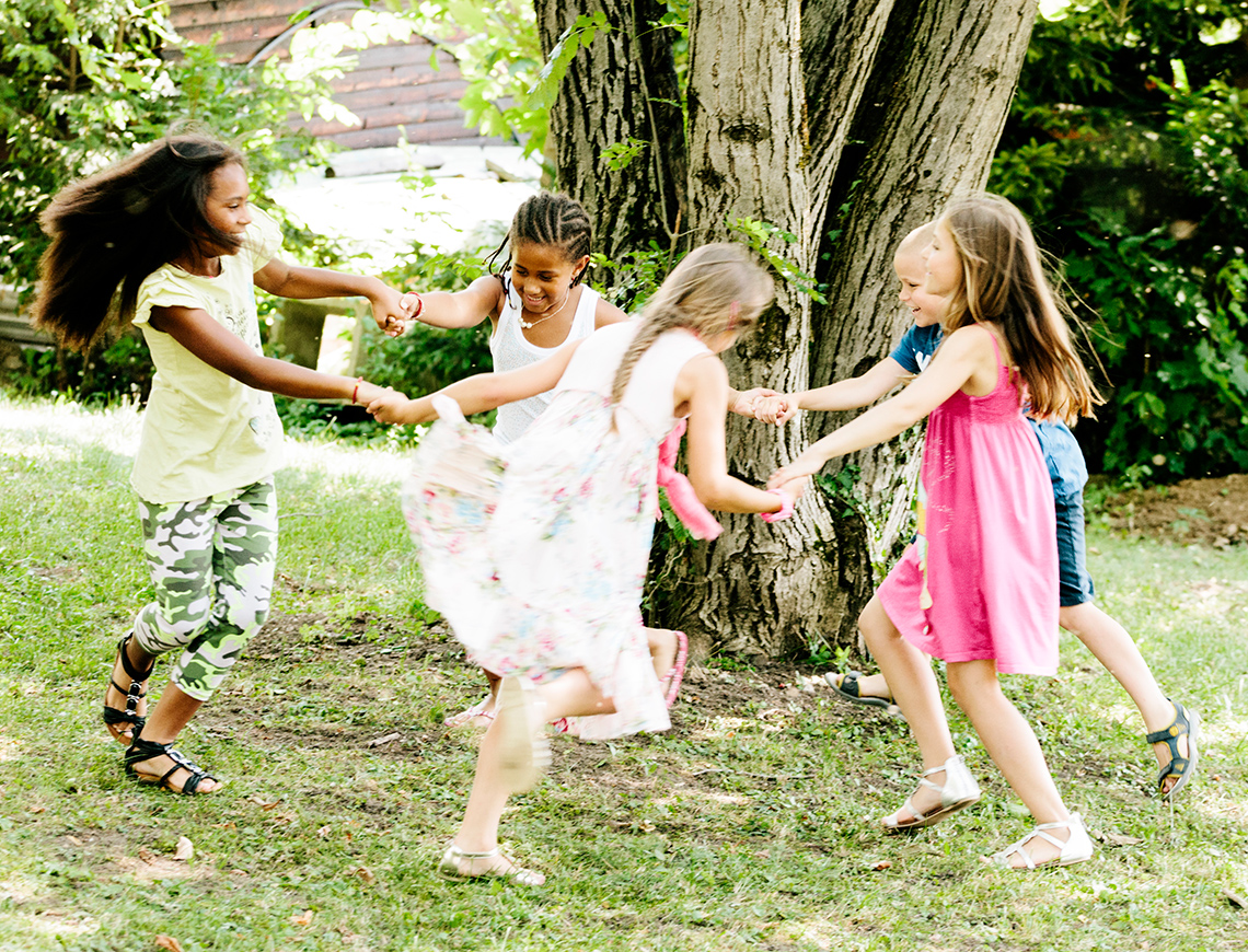 Three children are forming a circle while holding hands. They seem to be going round and round in a circle.
