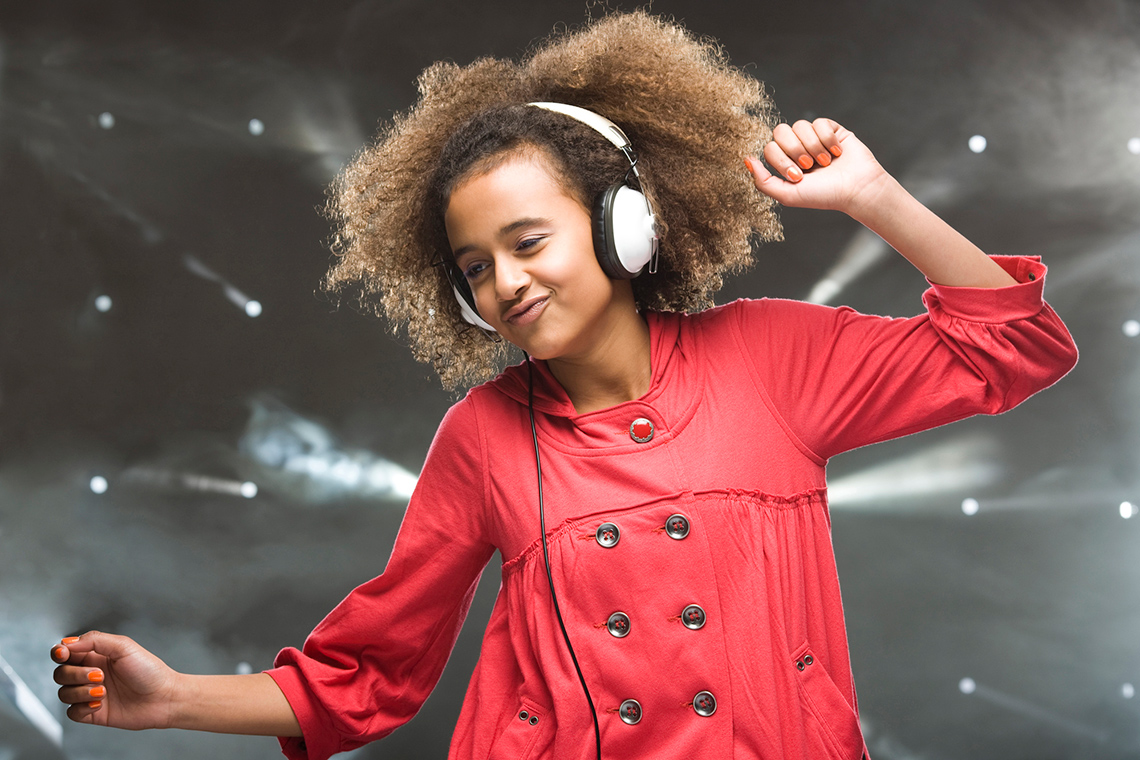 A dancer is smiling. Their head is slightly bowed, and they are standing at a high level with arms up and open.