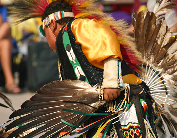 An indigenous person is dancing while wearing their traditional indigenous clothes.