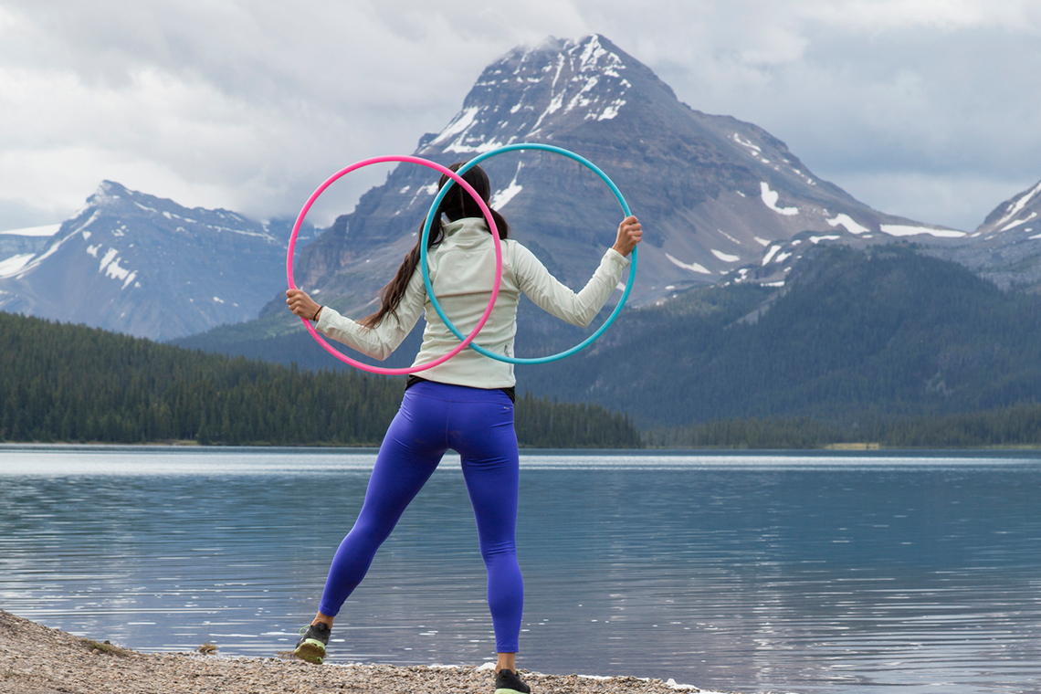 An indigenous person dancing with two hoops by the lake. Their reflection appears on the water surface.