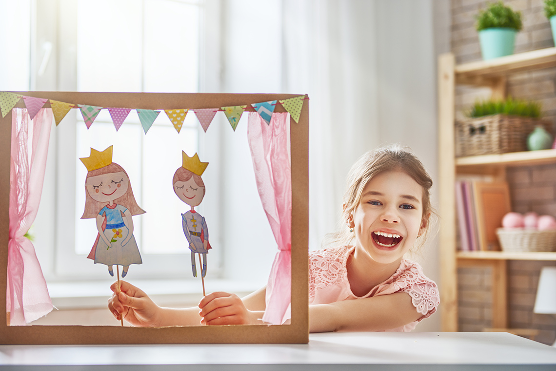 Puppet show being performed by a child with paper cut out dolls of a prince and princess. 