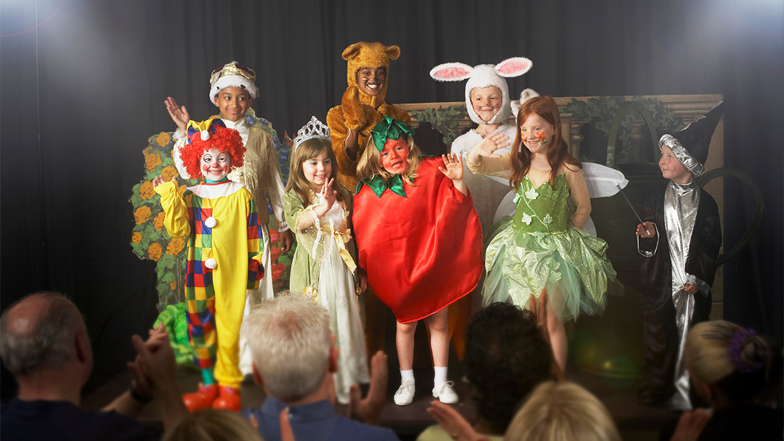 Children in costumes for a play. They are dressed as a tomato, a bear, a clown, a wizard, a fairy, a rabbit, a princess, and a prince.