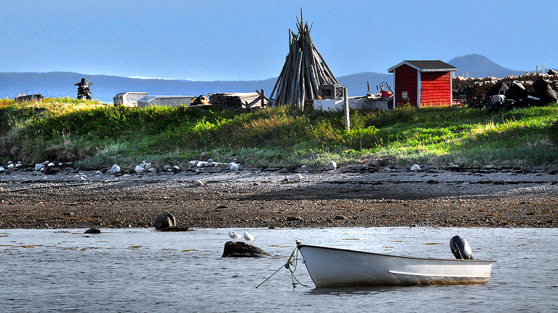 A coastal view of an area in the Nunatsiavut territory with a boat, several buildings, and an inukshuk.