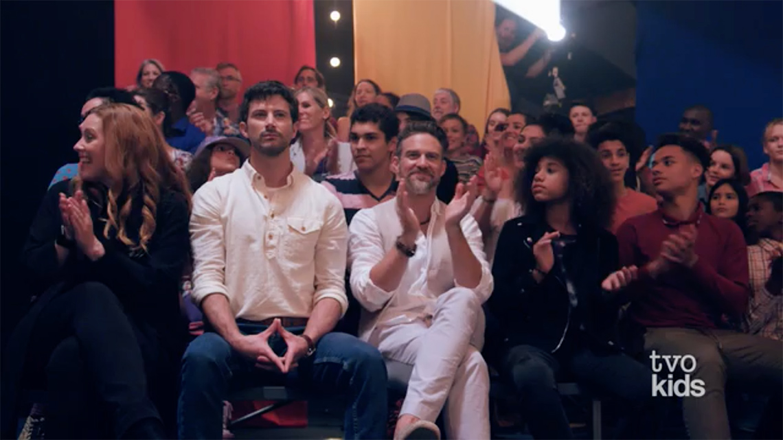 Screenshot from a video with some audience members clapping and smiling.