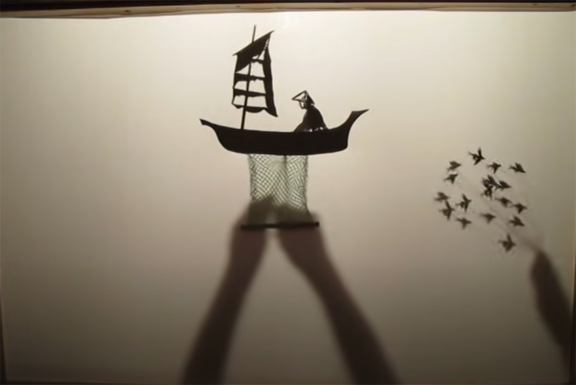 Shadow puppets of a fishing boat with sails up, nets down, and a person on it. Birds fly by.