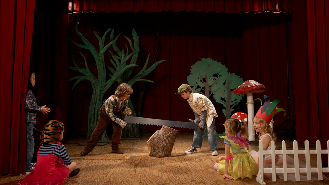 Two children acting as lumberjacks on stage, sawing a tree stump.