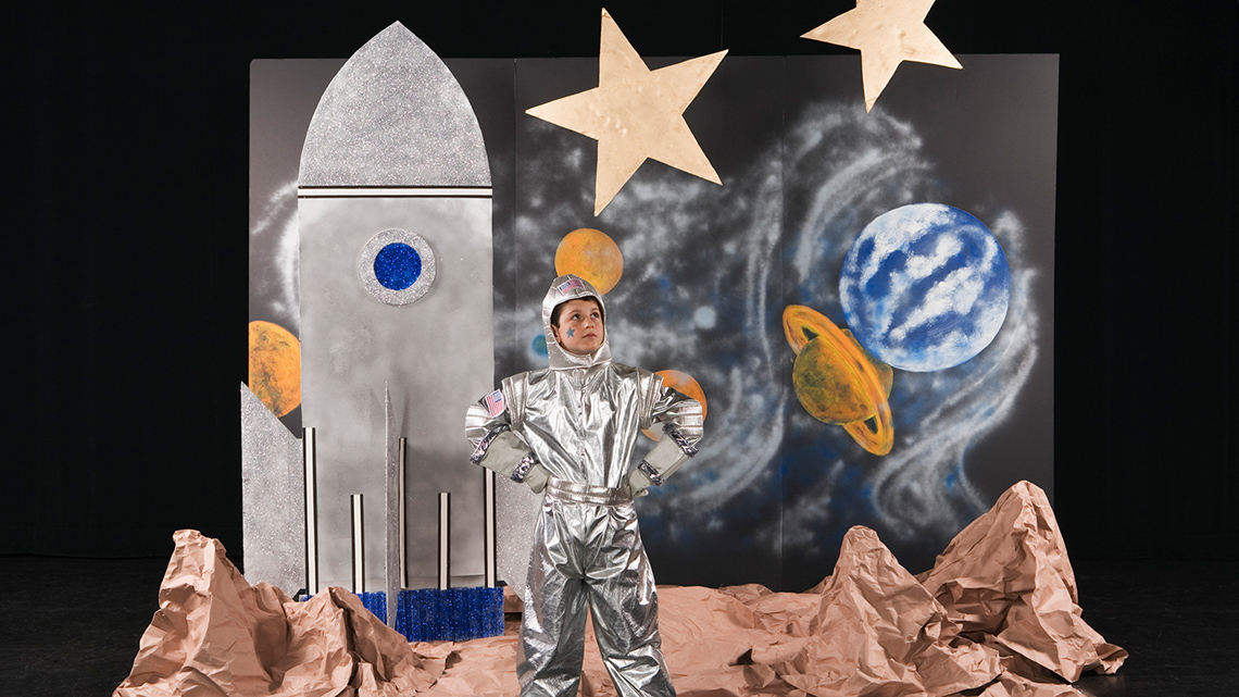 A child posing on stage wearing a spacesuit.