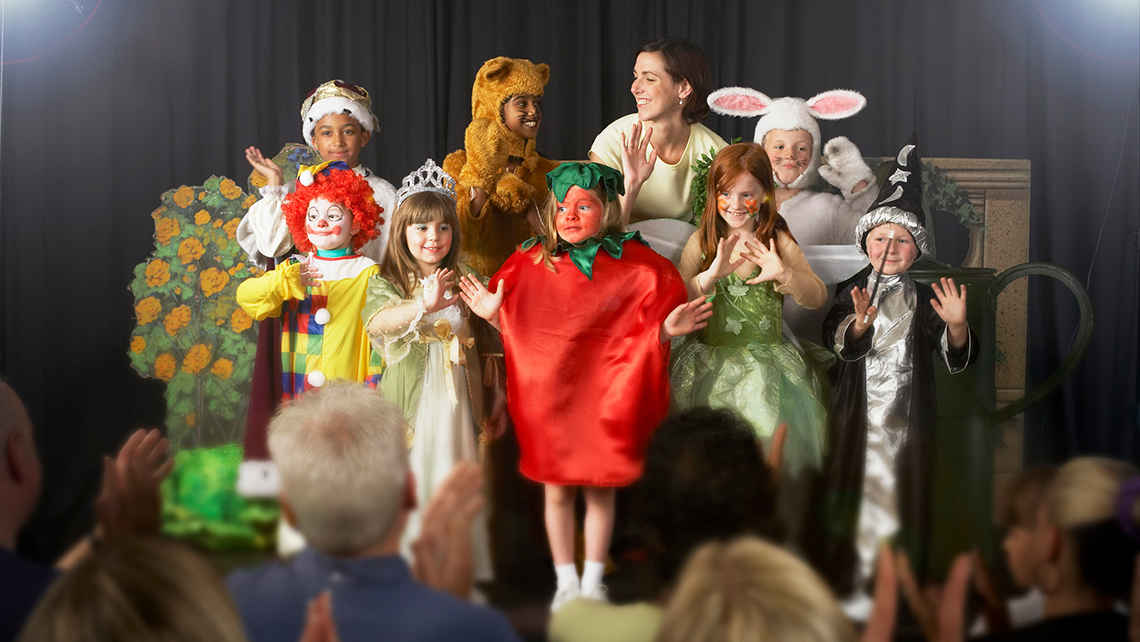 A group of children wearing costumes on stage and waving at the audience.