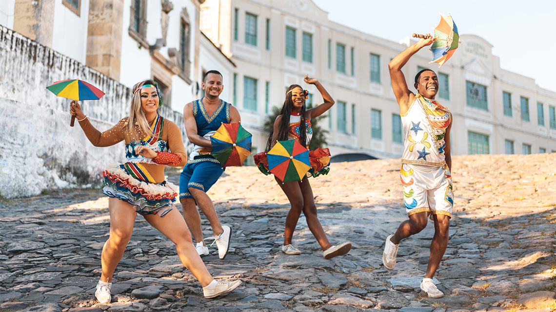 Four performers holding parasols and wearing Brazilian umbrella dance clothing.
