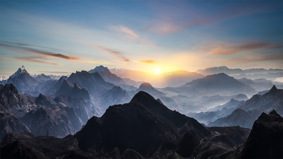 Silhouettes of mountains are surrounded by mist at sunrise.