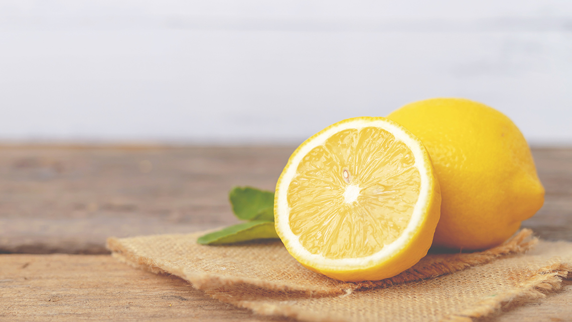 A cut half of a lemon is on a table beside another lemon.