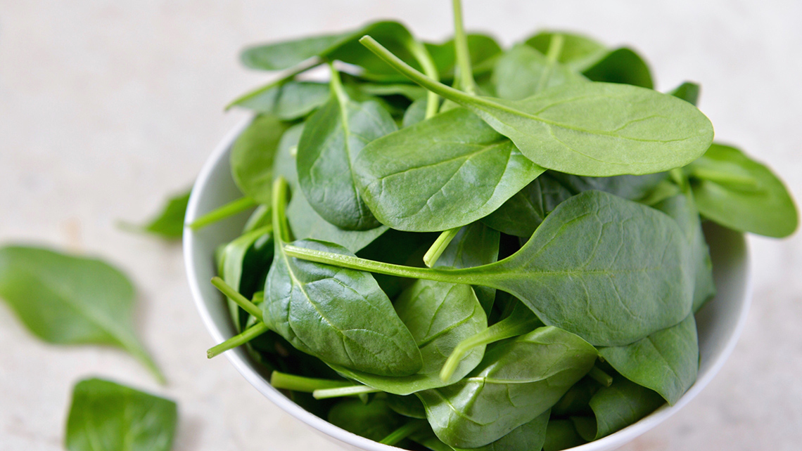 There is a bowl of spinach on a table.