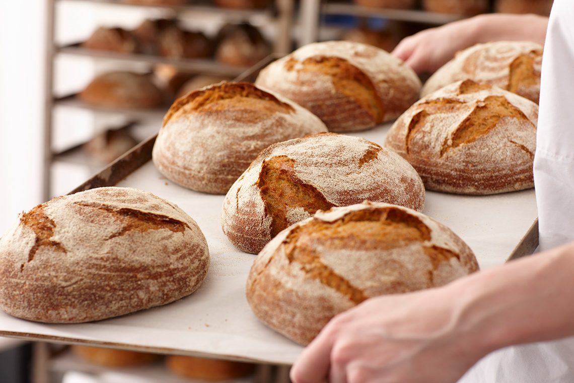 A person is holding a baking tray of freshly-baked bread loaves.