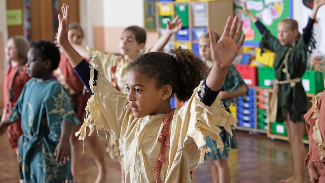 There are several kids dressed up in ragged robes. They are raising their hands together.