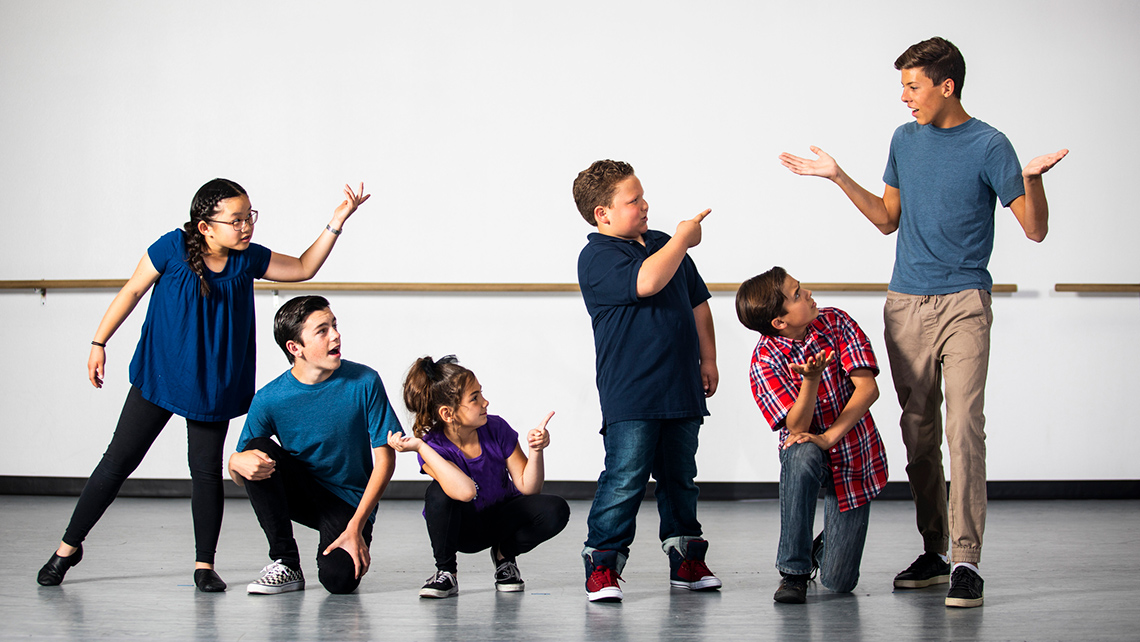 A group of kids doing dramatic poses. Some are crouched down and some have their hands raised. 