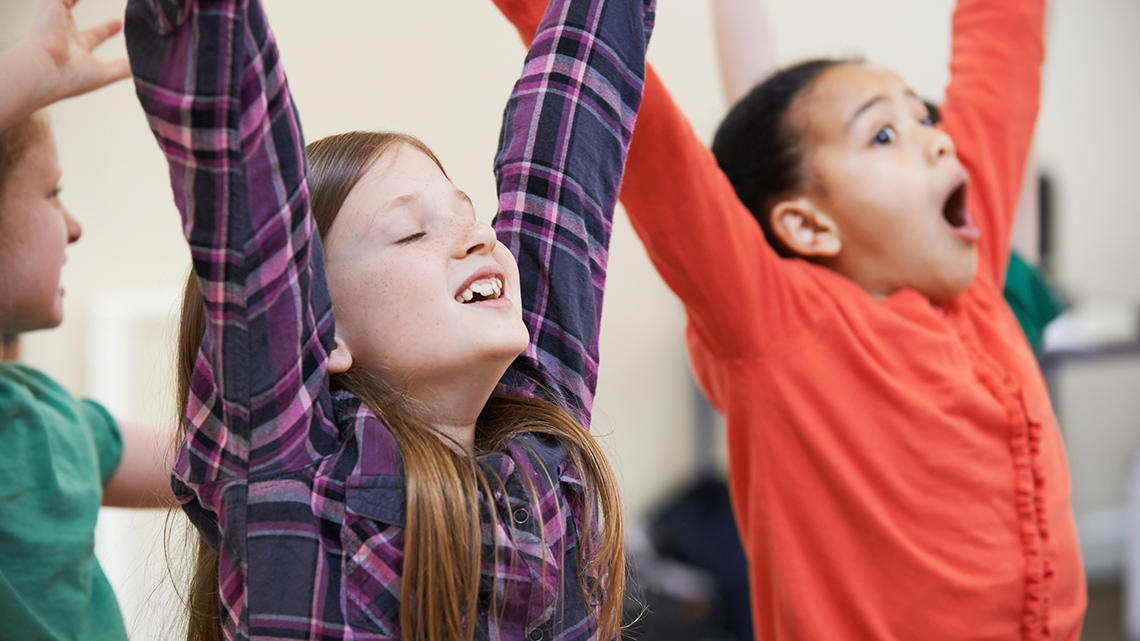 Several kids stand in a row, looking up, and waving their arms in the air.