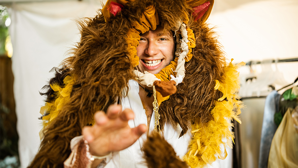A person dressed in lions costume, reaching their hand towards the screen. 