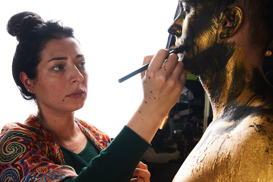 A make-up artist putting makeup on an actors face with a brush.