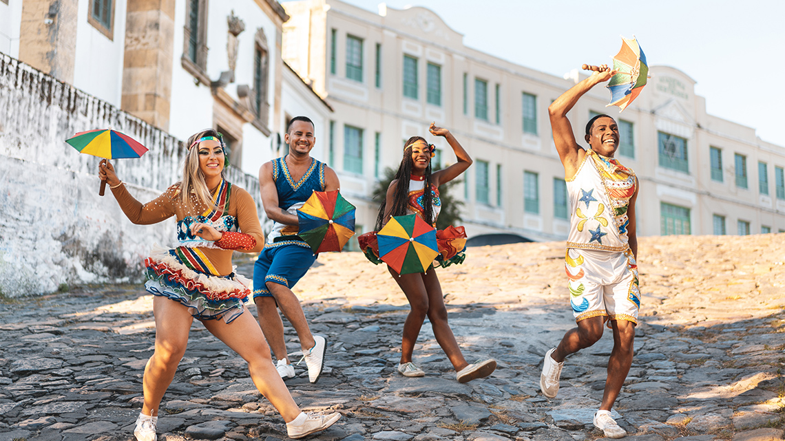 Four people dancing on a cobble street, all holding small umbrellas. 