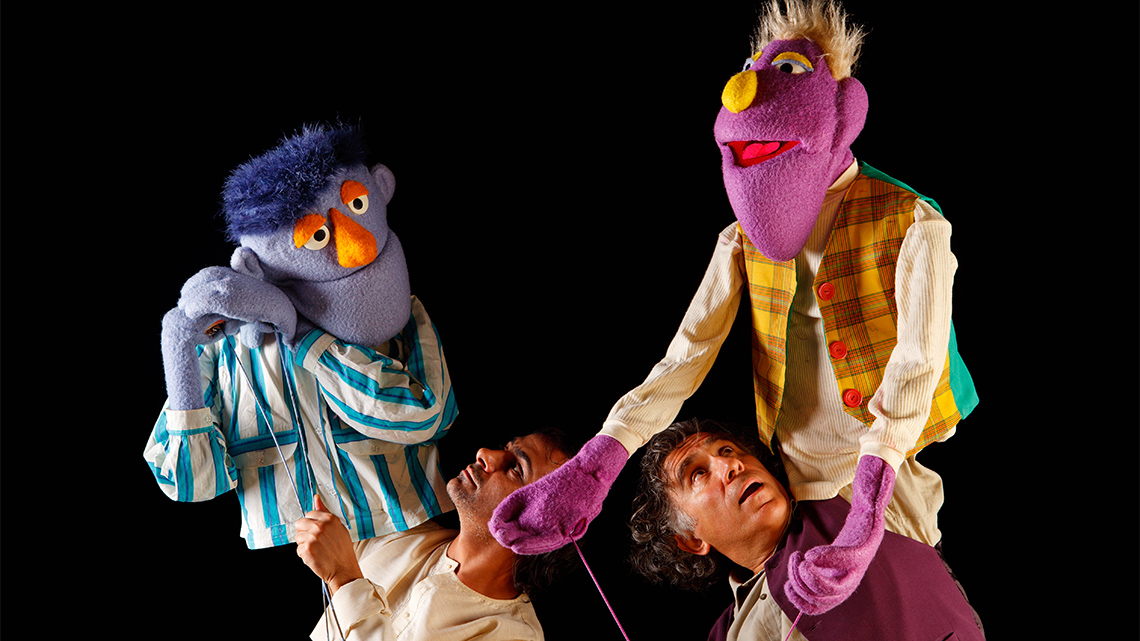 Two puppets being controlled by their puppeteers.